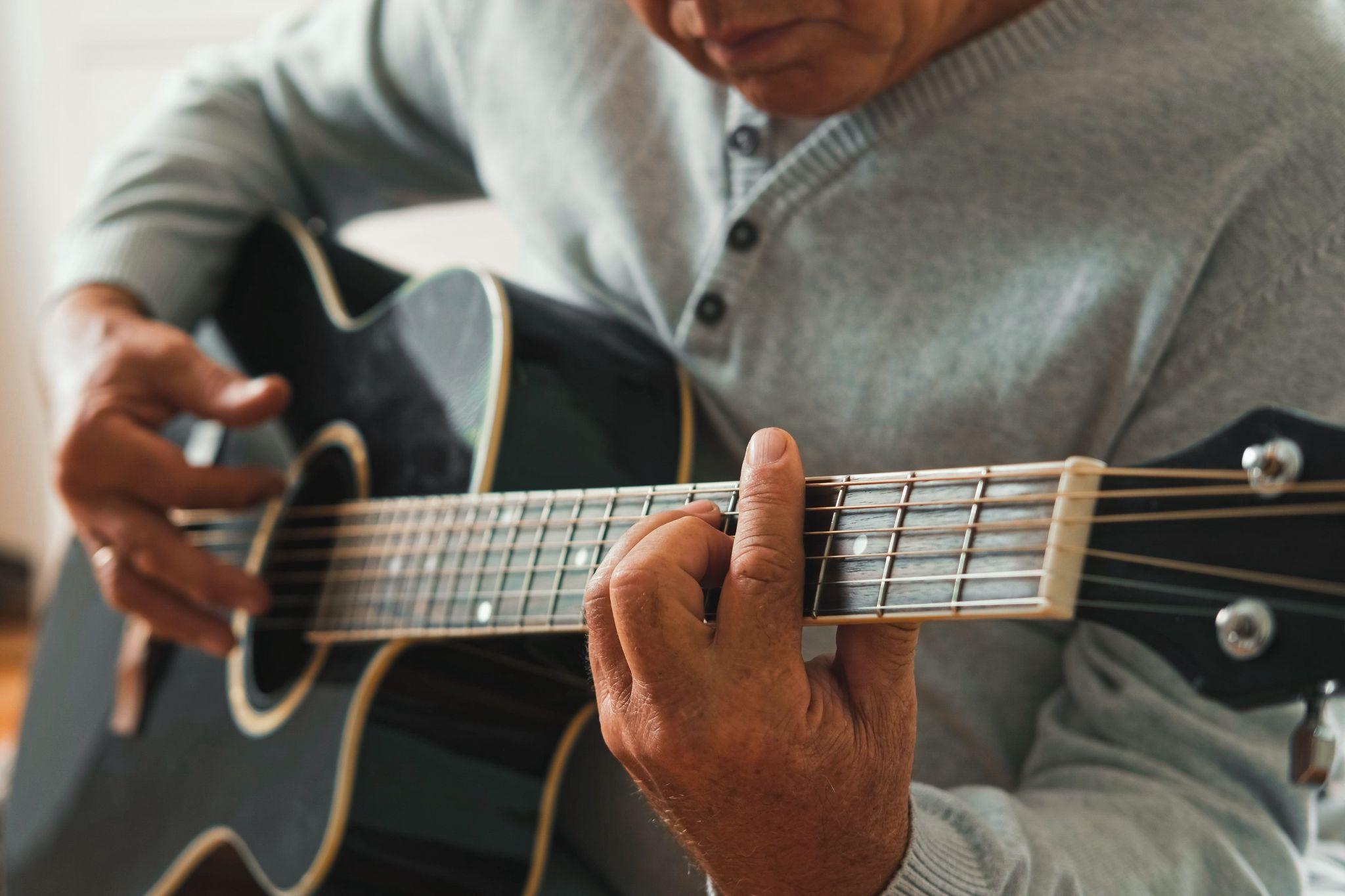An older adult sits down and plays the guitar to help support brain health.